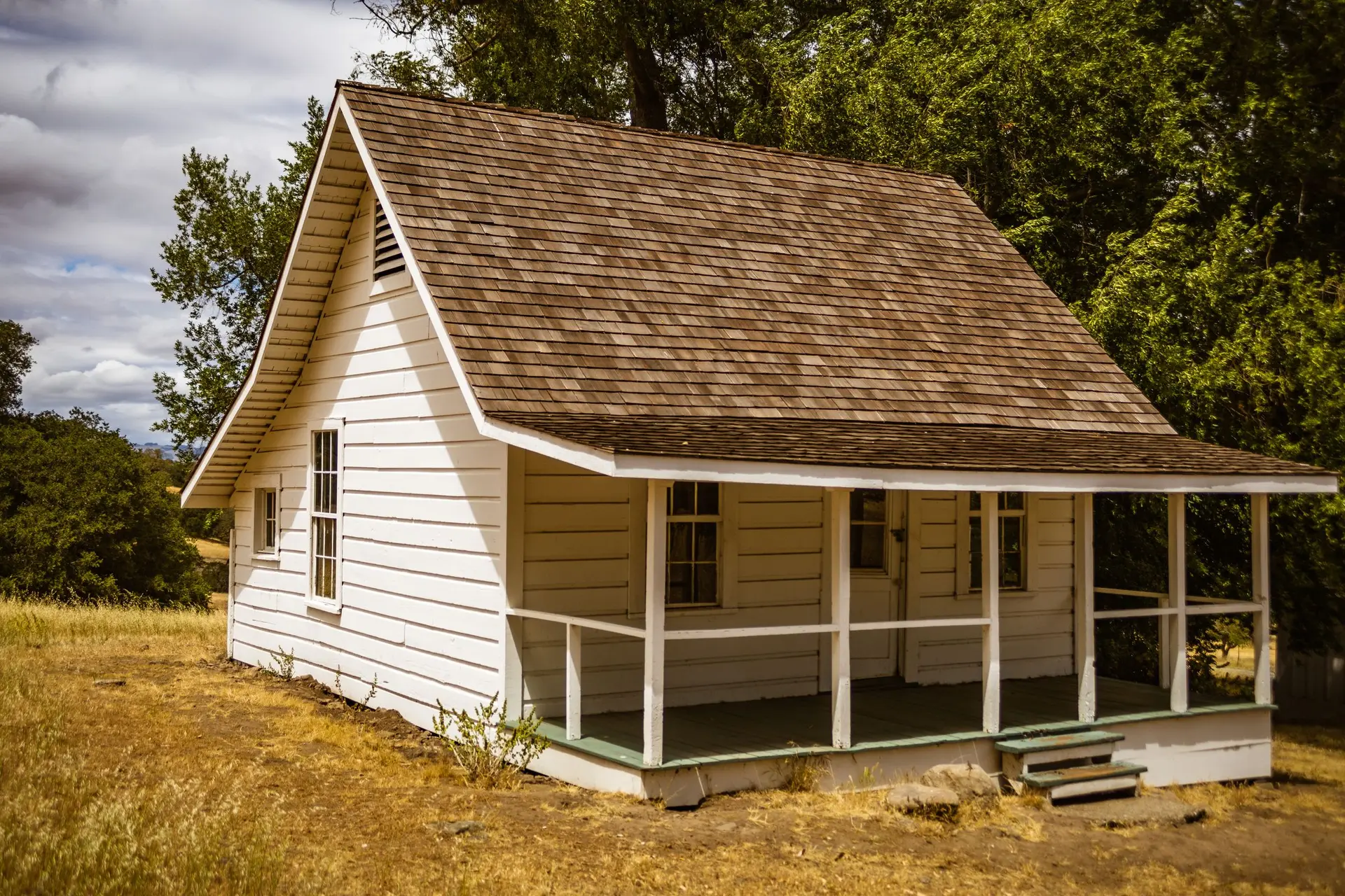 White wood cottage with a railed front porch and a cedar shingle roof